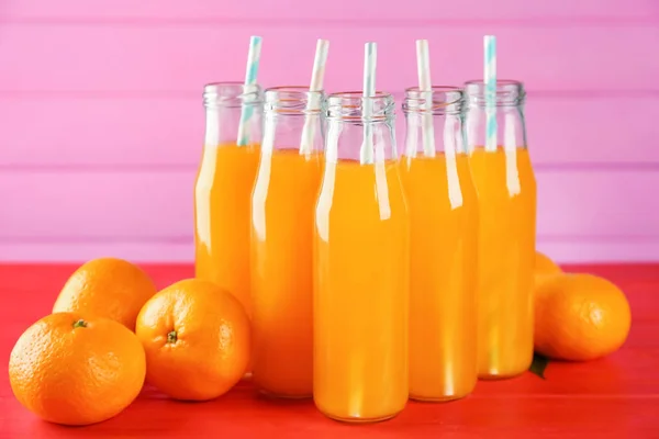 Flessen met verse sap van citrusvruchten en mandarijnen op tafel — Stockfoto