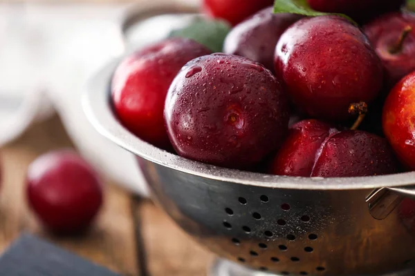 Colander with ripe juicy plums on table, closeup — Stock Photo, Image