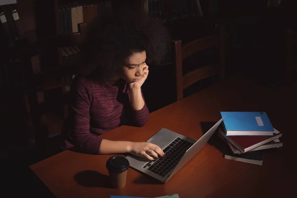 Student afro-american cu laptop care studiază în bibliotecă noaptea târziu — Fotografie, imagine de stoc