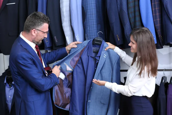 Unga shop assistent hjälpa mannen att välja kostym i butik — Stockfoto