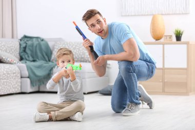 Sevimli çocuk ve babası evde oyuncak silahlarla oynayan