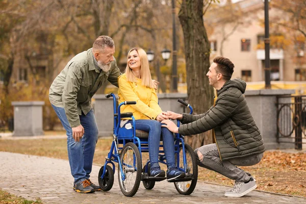 Woman in wheelchair with her family outdoors on autumn day