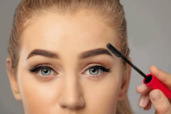 Young woman undergoing eyebrow correction procedure on grey background, closeup