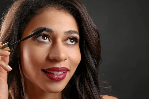 Attractive African-American woman with long eyelashes using mascara on black background. Eyelash extensions