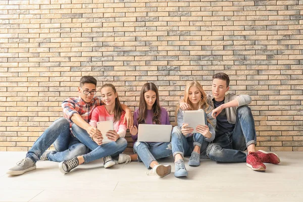 Adolescenti con dispositivi moderni seduti al piano vicino alla parete — Foto Stock