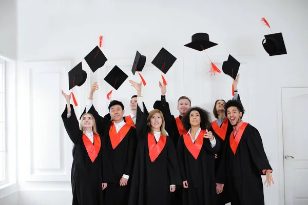 Gelukkig studenten in de Bachelor in gewaden gooien mortarboards binnenshuis. Graduatiedag — Stockfoto
