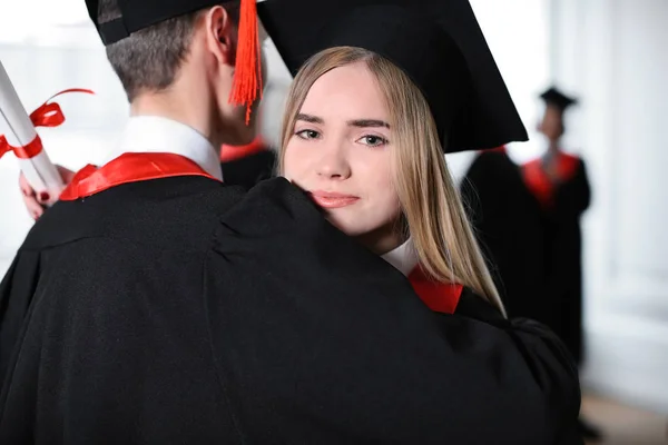 Gelukkig studenten in de Bachelor in gewaden knuffelen binnenshuis, graduatie dag — Stockfoto