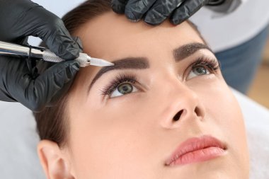 Young woman undergoing procedure of eyebrow permanent makeup in beauty salon, closeup clipart