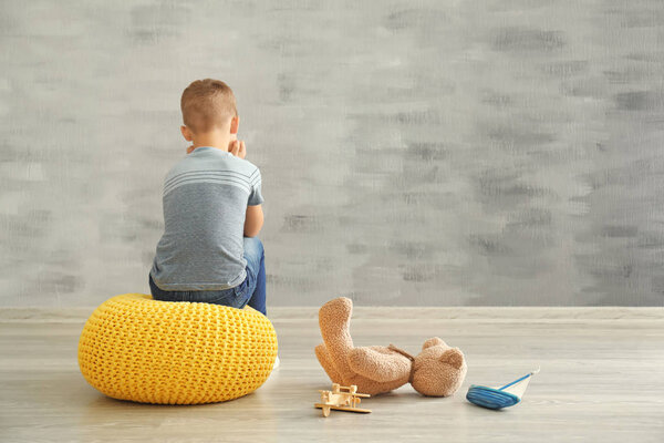 Little boy sitting near wall in empty room. Autism concept