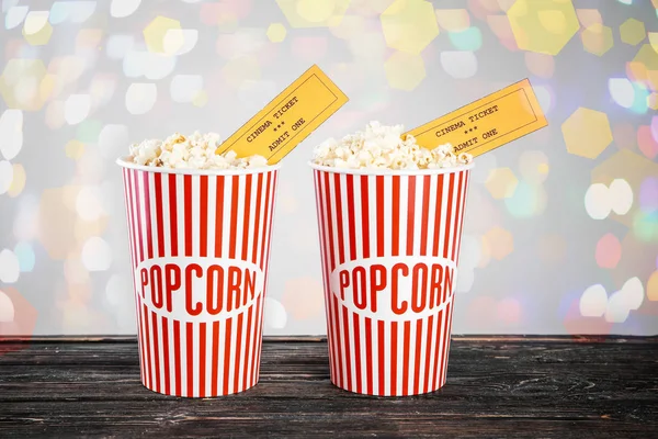 Paper cups of tasty popcorn with cinema tickets and blurred lights on background