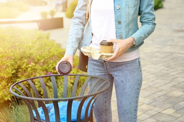 Woman throwing paper cup in litter bin outdoors. Recycling concept