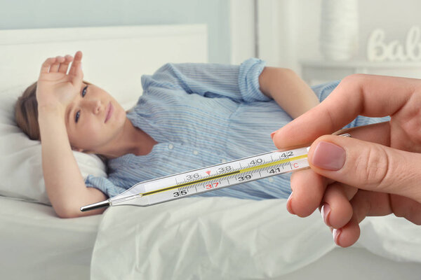 Врач держит термометр с высокой температурой и больная беременная женщина лежит на кровати дома
