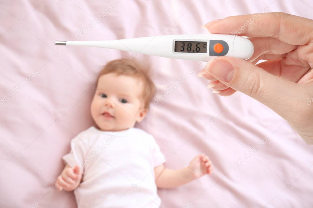 Woman holding thermometer with high temperature and sick baby lying on bed
