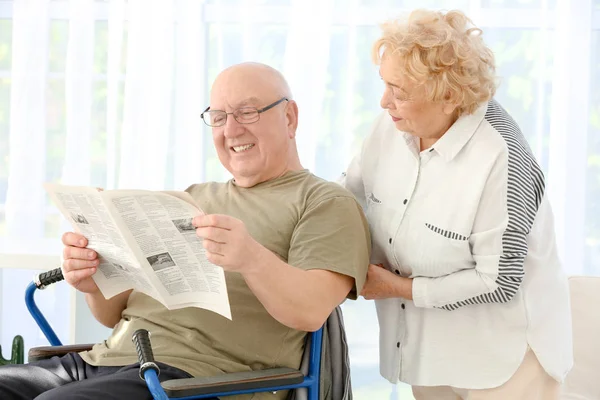 Senior férfi kerekesszékes és nő olvasó újság home Care — Stock Fotó