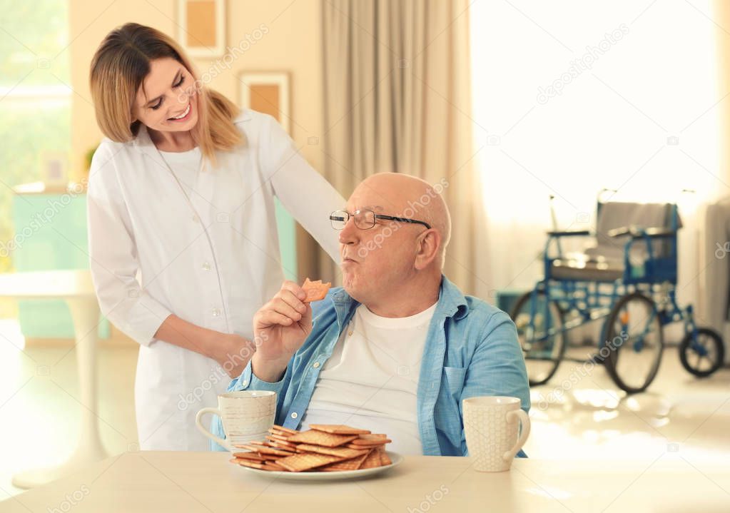 Senior man talking with nurse while having breakfast at care home