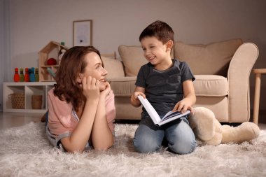 Sevimli küçük çocuk annesi okuma kitabında evde akşam ile