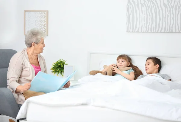 Niñera mayor leyendo libro a niño pequeño en el interior — Foto de Stock