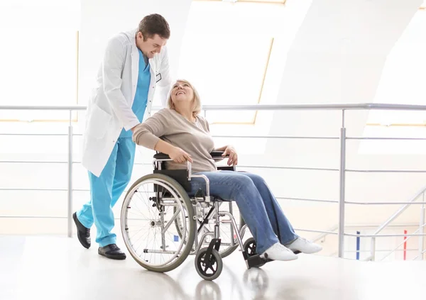 Male doctor taking care of mature woman in wheelchair indoors — Stock Photo, Image