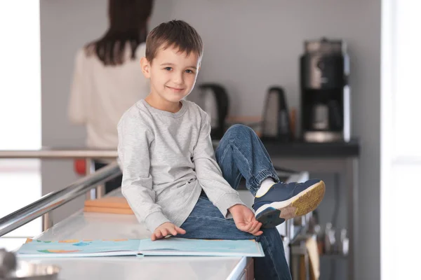 Cute little boy reading book in kitchen — Stock Photo, Image