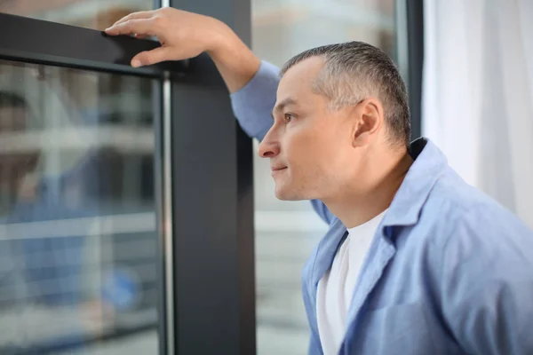 Volwassen man in casual kleding in de buurt van venster thuis — Stockfoto