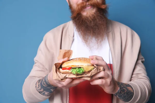 Mann mit leckerem Burger vor farbigem Hintergrund — Stockfoto