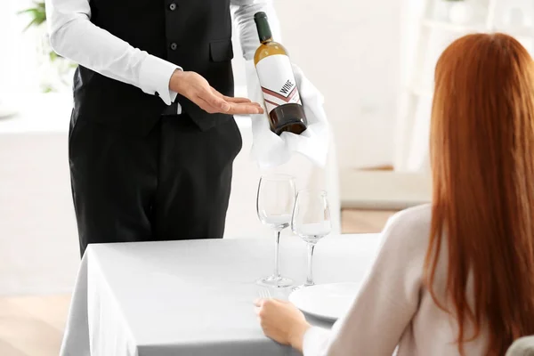 Waiter offering bottle of wine to client in restaurant