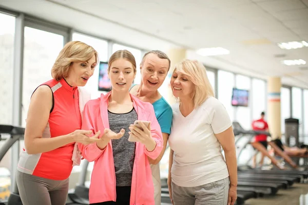 Junger Trainer mit Telefon und Gruppe reifer Frauen in modernem Fitnessstudio — Stockfoto