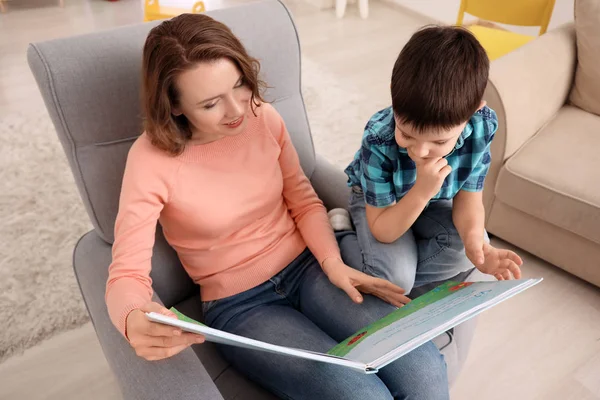 Милый маленький мальчик с матерью, читающей книгу дома вечером. — стоковое фото