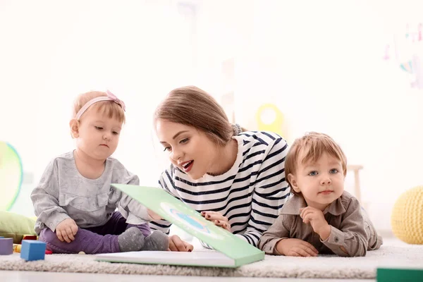 Young nanny reading book to cute little children on bed — Stock Photo, Image