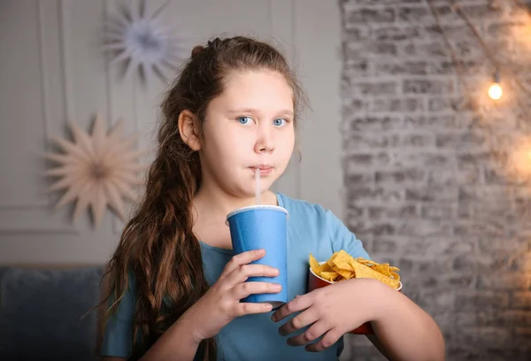 Overweight girl with chips and drink indoors