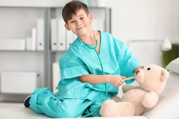 Schattige kleine jongen in dokter uniforme spelen met speelgoed beer in ziekenhuis — Stockfoto