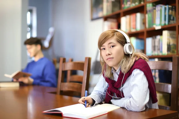 Estudiante asiático con auriculares estudiando en la biblioteca — Foto de Stock