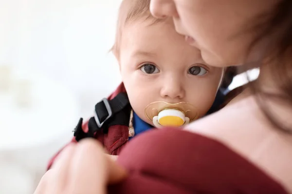 Молода жінка з дитиною в слінгу говорить на мобільний телефон в приміщенні — стокове фото