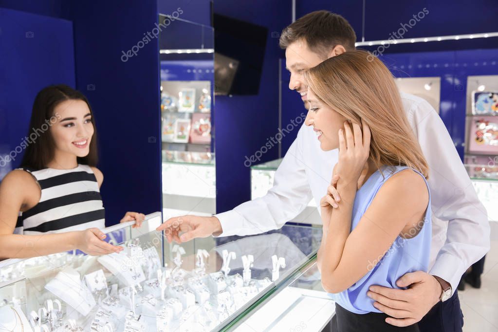 Young shop assistant helping couple choose jewelry in store