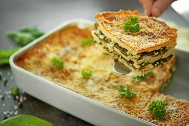 Spatula ıspanaklı lazanya parçası ile yemek pişirme üzerinde tutan kadın