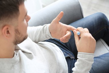 Diyabetli adam evde tükenmez kalemle kan örneği alıyor.