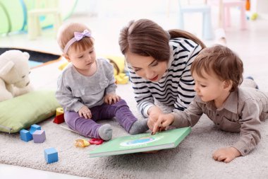 Cute little girl with young nanny at table, indoors clipart