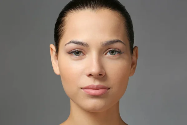 Young woman with natural eyebrows on grey background