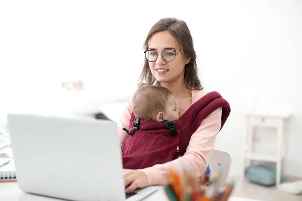 Mujer Joven Con Bebé Portador Ergo Utilizando Ordenador Portátil Interior — Foto de Stock