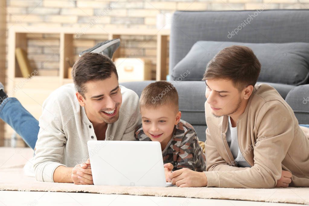 Male gay couple and adopted boy with laptop on floor at home