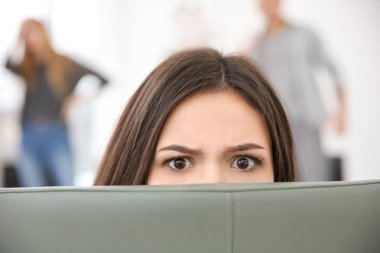 Woman hiding behind chair during group therapy, indoors clipart