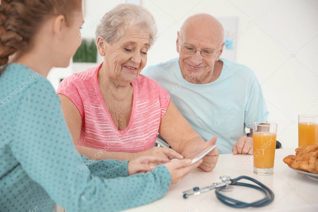 Young caregiver teaching senior couple to handle with tablet computer at home