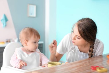 Young nanny feeding cute little girl, indoors clipart