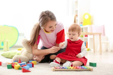 Young nanny feeding cute little girl, indoors clipart