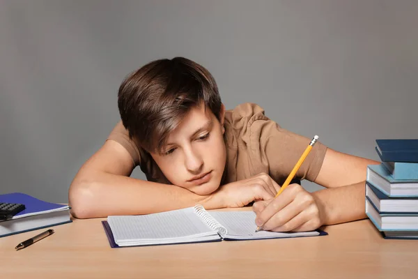 Cansado Adolescente Chico Haciendo Tarea Contra Gris Fondo — Foto de Stock