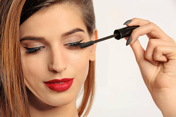 Woman applying mascara on her eyelashes against white background