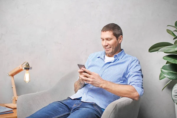Young man in casual clothes using cell phone at home