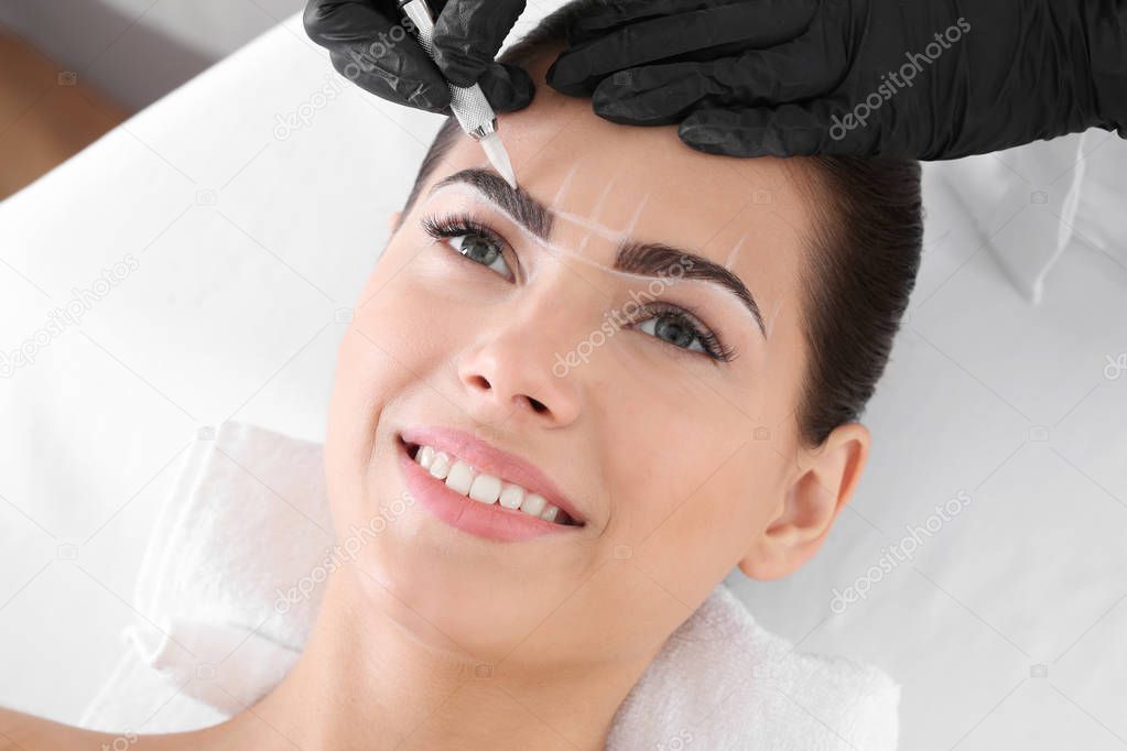 Young woman undergoing procedure of eyebrow permanent makeup in beauty salon