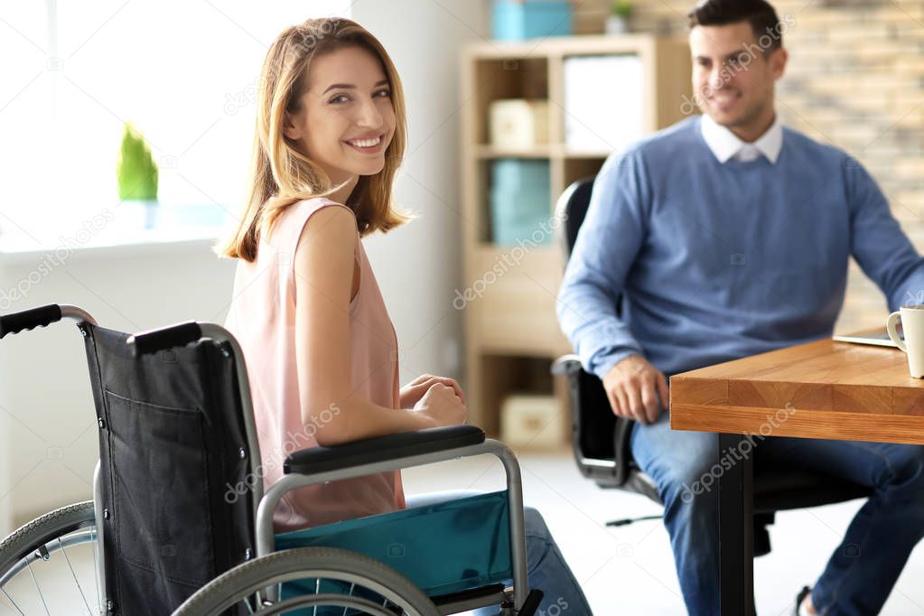 Young woman in wheelchair with colleague at workplace