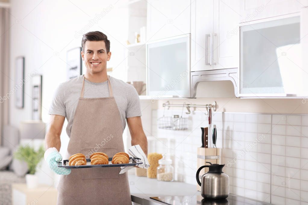 Man holding baking tray with delicious homemade croissants in kitchen